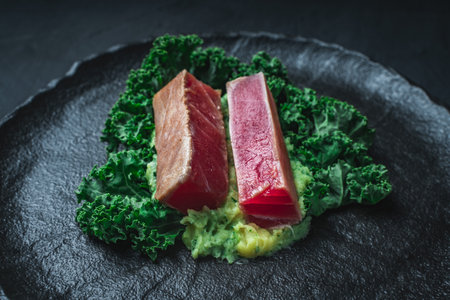 The tuna slices are lightly fried on mashed potatoes with spinach and Kale lettuce on a black mica plate and background. The concept of healthy eating. Original serving of the dish. High quality photoの写真素材