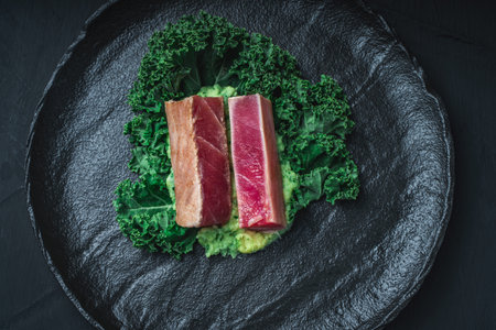 The tuna slices are lightly fried and served on mashed potatoes with spinach and Kale lettuce on a black mica plate on a dark background. The concept of healthy eating. Top view. High quality photoの写真素材