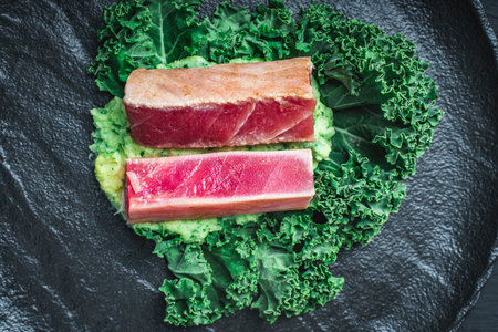 The tuna slices are lightly fried and served on mashed potatoes with spinach and Kale lettuce on a black mica plate on a dark background. The concept of healthy eating. Top view. High quality photoの写真素材