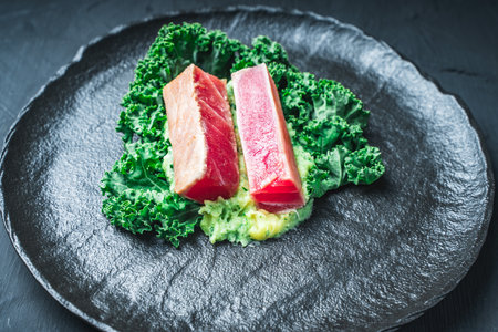 The tuna slices are lightly fried on mashed potatoes with spinach and Kale lettuce on a black mica plate and background. The concept of healthy eating. Original serving of the dish. High quality photoの写真素材