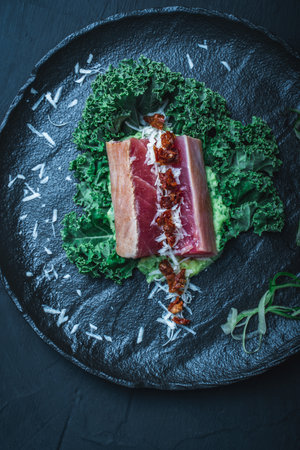 Tuna served with mashed potatoes, kale salad, sun-dried tomatoes and cheese on a black plate, background. Original, restaurant serving of fish. Dietary Nutrition Concept.Top view. High quality photoの写真素材