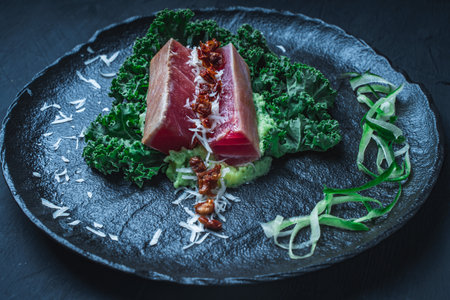Tuna served with mashed potatoes, kale salad, sun-dried tomatoes and cheese on a black plate, background. Original, restaurant serving of fish. Dietary Nutrition Concept.Top view. High quality photoの写真素材