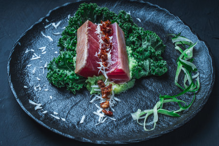 Tuna served with mashed potatoes, kale salad, sun-dried tomatoes and cheese on a black plate, background. Original, restaurant serving of fish. Dietary Nutrition Concept.Top view. High quality photoの写真素材