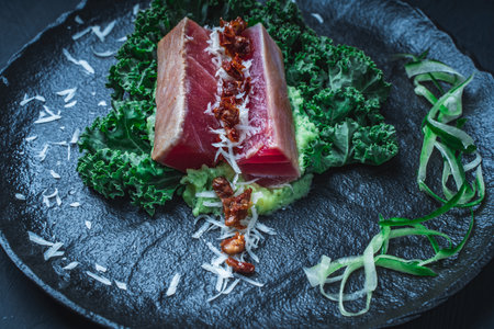 Tuna served with mashed potatoes, kale salad, sun-dried tomatoes and cheese on a black plate, background. Original, restaurant serving of fish. Dietary Nutrition Concept.Top view. High quality photoの写真素材