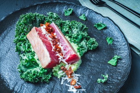 Tuna served with mashed potatoes, kale salad, sun-dried tomatoes and cheese on a black plate, background. Original, restaurant serving of fish. Dietary Nutrition Concept.Top view. High quality photoの写真素材