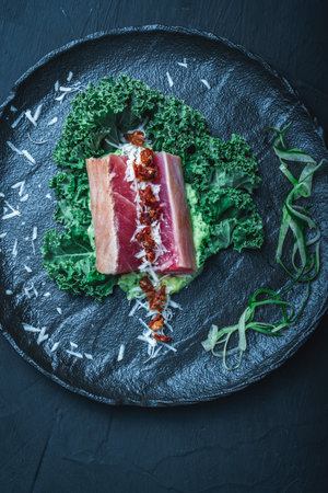 Tuna served with mashed potatoes, kale salad, sun-dried tomatoes and cheese on a black plate, background. Original, restaurant serving of fish. Dietary Nutrition Concept.Top view. High quality photoの写真素材