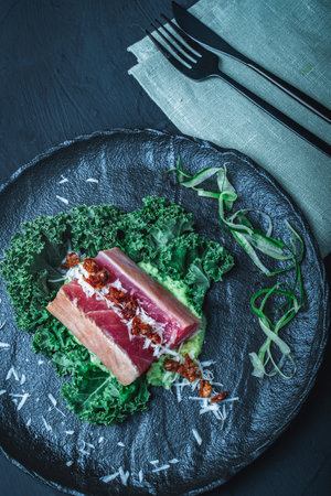 Tuna served with mashed potatoes, kale salad, sun-dried tomatoes and cheese on a black plate, background. Original, restaurant serving of fish. Dietary Nutrition Concept.Top view. High quality photoの写真素材