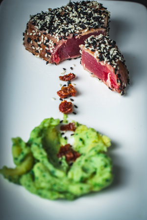 Sliced organic grilled tuna fillet, topped with sesame seeds with spinach puree and sun-dried tomatoes on a black mica serving board. Selected focus. Vertical Photo. High quality photoの写真素材
