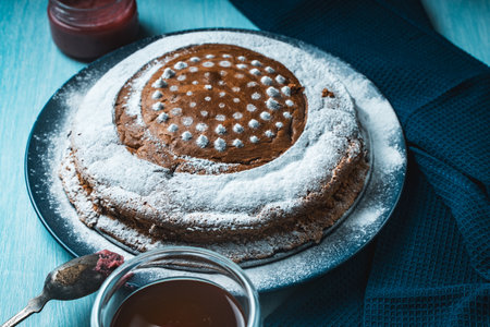 Delicious, homemade pie sprinkled with powdered sugar on a blue plate and background with a napkin and tea with cherries on the table. High quality photoの写真素材