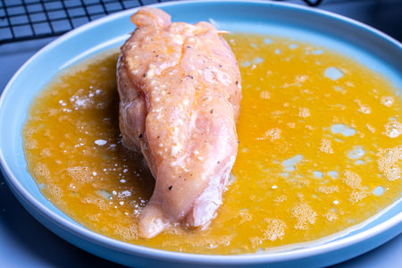 Chicken meat rolled in flour is dipped in egg yolk in a blue plate. French Gordon Blue recipe. High quality photoの写真素材