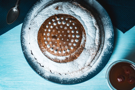 Delicious, homemade pie sprinkled with powdered sugar on a blue plate and background with a napkin and tea with cherries on the table. High quality photoの写真素材