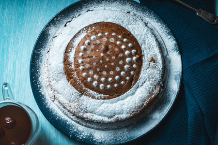 Delicious, homemade pie sprinkled with powdered sugar on a blue plate and background with a napkin and tea with cherries on the table. High quality photoの写真素材