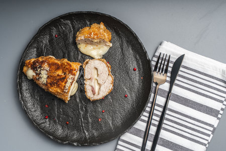 Pieces of chicken cutlet Cordon Bleu with bacon and cheese according to a traditional French recipe on a black mica plateon a gray background with napkin and cutlery. Space for text. High quality photoの写真素材
