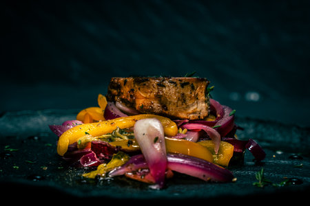 Slice of roasted pork tenderloin with vegetables, pink onion and yellow pepper on a black plate on a dark background. Beautiful, restaurant presentation of the dish. High quality photoの写真素材