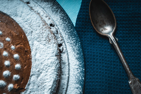 Delicious homemade pie, sprinkled with powdered sugar, on a blue plate with a blue napkin and a spoon. Top view, close-up. High quality photoの写真素材