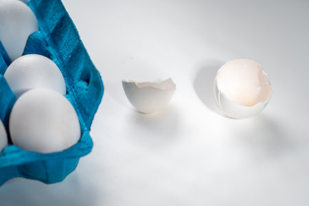 A white eggshell and a blue box with whole eggs on a white background. Space for text. High quality photoの写真素材