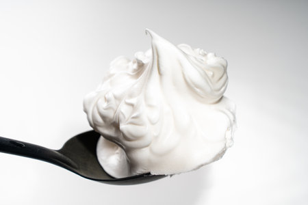 Egg whites or meringues whipped with sugar on a black spoon on a white background. Close-up. Space for text. High quality photoの写真素材