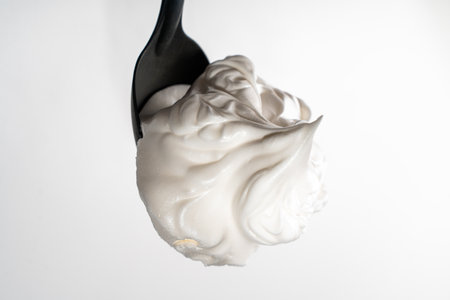 Egg whites or meringues whipped with sugar on a black spoon on a white background. Close-up. Space for text. High quality photoの写真素材