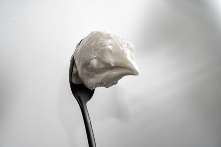 Egg whites or meringues whipped with sugar on a black spoon on a white background. Close-up. Space for text. High quality photoの写真素材
