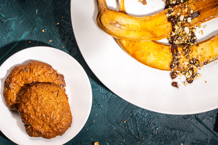 Cookies on a white plate and flambeed bananas with nuts and chocolate on a dark green background. Top view, close-up, space for text. High quality photoの写真素材