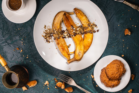 Bananas flambe on a white plate with nuts and chocolate on a table with coffee and a cezve on a dark background with a knife and fork. Top view. Restaurant serving dessert High quality photoの写真素材