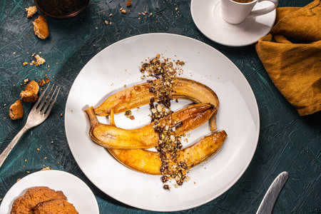 Bananas flambe on a white plate with nuts and chocolate on a table with coffee and a cezve on a dark background with a knife and fork. Top view. Restaurant serving dessert High quality photoの写真素材