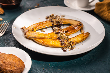 Bananas flambe on a white plate with nuts and chocolate on a table with coffee and a cezve on a dark background with a knife and fork. Restaurant serving dessert High quality photoの写真素材