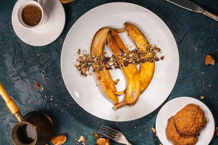 Bananas flambe on a white plate with nuts and chocolate on a table with coffee and a cezve on a dark background with a knife and fork. Top view. Restaurant serving dessert High quality photoの写真素材