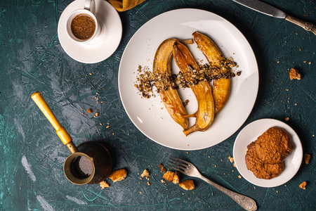 Bananas flambe on a white plate with nuts and chocolate on a table with coffee and a cezve on a dark background with a knife and fork. Top view. Restaurant serving dessert High quality photoの写真素材