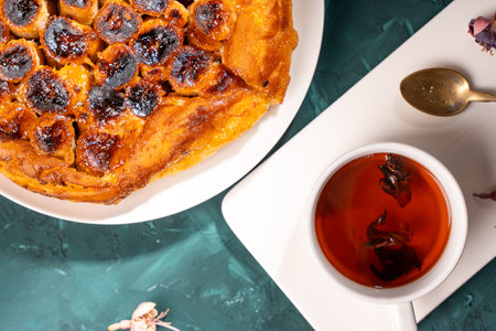 Banana Tarte Tatin on a white plate on a dark green table with a cup of tea. Close-up. Top view. High quality photoの写真素材