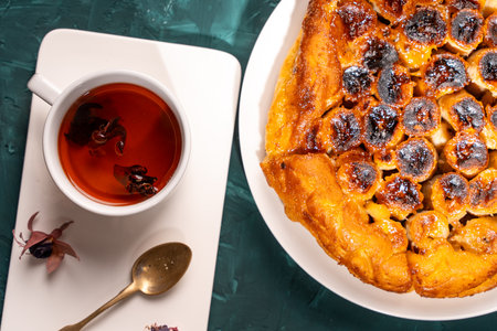 Banana Tarte Tatin on a white plate on a dark green table with a cup of tea. Close-up. Top view. High quality photoの写真素材