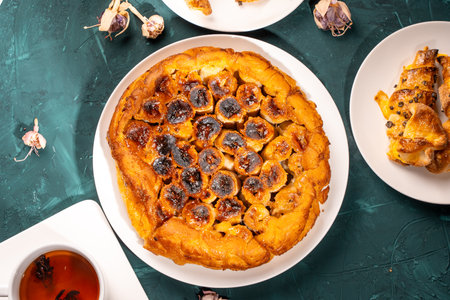 Traditional homemade banana caramel pie. French Tarte Tatin on a white plate with a cup of tea on a green, emerald background. Top view. Close-up. High quality photoの写真素材