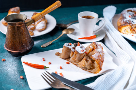 A slice of banana pie with hot chili peppers and coffee cooked in a cezve on a dark green background. French Tarte Tatin and handmade croissants on the table. High quality photoの写真素材