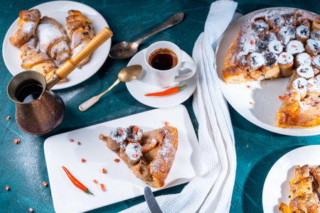 Homemade cakes, banana tarte, tatin and croissants on a dark green background with a cup of coffee brewed in a cezve and red chili peppers. High quality photoの写真素材