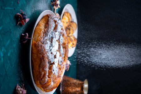 Banana Tarte Tatin is sprinkled with powdered sugar on a white plate on a dark background. The...
