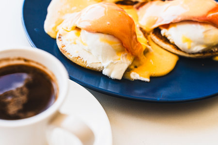 Egg Benedict with salmon and hollandaise sauce on a blue plate with a cup of freshly brewed coffee. selected focus. Concept: healthy breakfast. High quality photoの写真素材