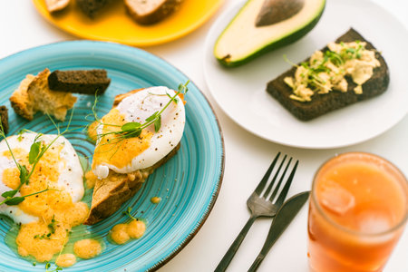 Rye bread toast with avocado and poached eggs on a blue plate on a light background. Selected focus. Healthy dietary breakfast. High quality photoの写真素材