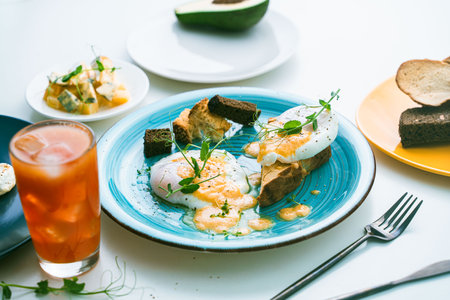 Poached eggs with sauce on toast with crouton on a turquoise plate, next to a glass of orange juice and cutlery. High quality photoの写真素材