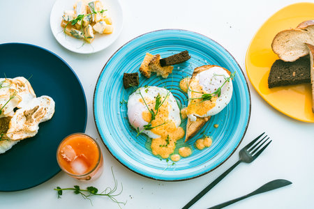 Poached eggs with hollandaise sauce on toast with crouton on a turquoise plate, next to a glass of...