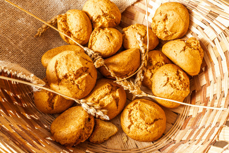 Freshly baked buns in a wicker basket with ears of wheat. Close-up. Selected focus. High quality photoの写真素材