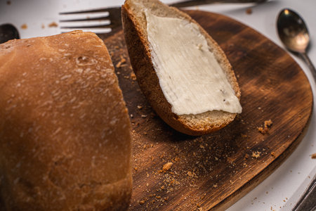A slice of bread with butter and a cut loaf on a wooden board on a white table and background. High quality photoの写真素材