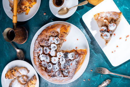 Banana tarte Tatin on a turquoise table with coffee brewed in a cezve and croissants. A slice of French dessert garnished with freeze-dried strawberries. View from above. High quality photoの写真素材