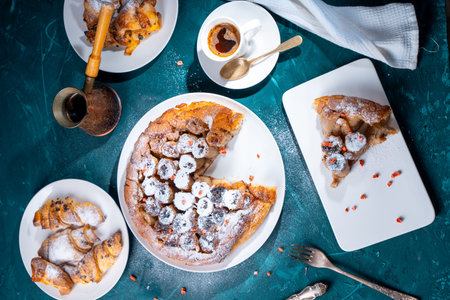 Banana tarte Tatin on a turquoise table with coffee brewed in a cezve and croissants. A slice of French dessert garnished with freeze-dried strawberries. View from above. High quality photoの写真素材