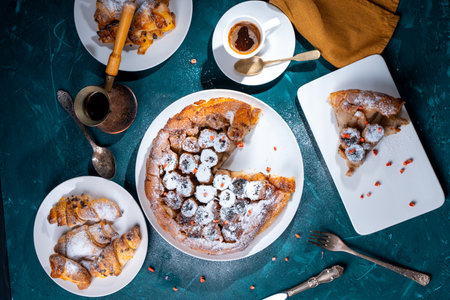 Banana tarte Tatin on a turquoise table with coffee and croissants. A slice of French dessert garnished with freeze-dried strawberries. View from above. High quality photoの写真素材