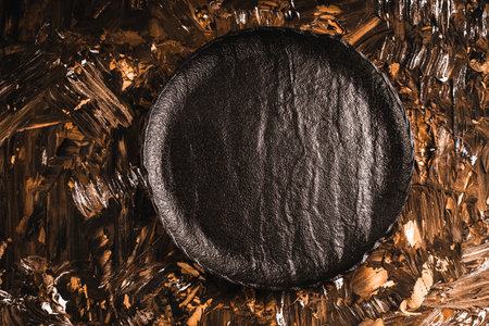 A black mica plate is empty on a brown gold background. Top view, flat layout, close-up. High quality photoの写真素材
