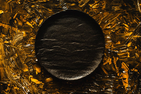 A black mica plate is empty on a brown gold background. Top view, flat layout, close-up. High quality photoの写真素材