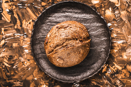Rye bread or bun on a black mica board on a brown textured background. Close-up. Space for text....