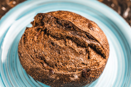 A loaf of rye bread on a turquoise or blue plate on a brown background. Close-up. Top view, Space...