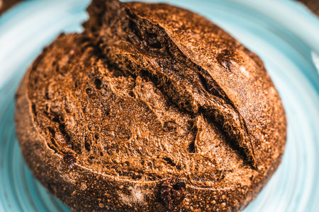 A loaf of rye bread on a turquoise or blue plate on a brown background. Close-up. Top view, Space...