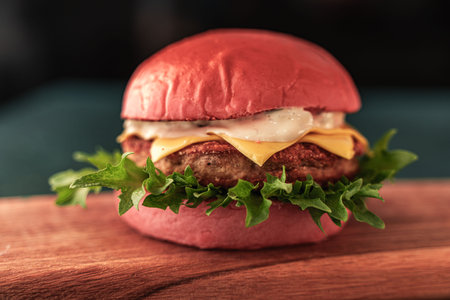 Pink burger with cheese and beef or fish patty with lettuce and sauce on a wooden board and dark background. Close-up. Space for text. High quality photoの写真素材